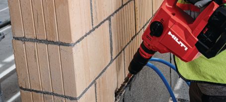 Herramienta de perforación en uso en una pared con bloques de construcción.