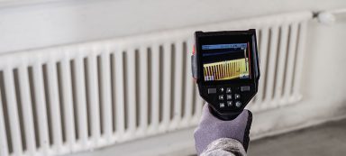 Termómetro infrarrojo apuntando a un radiador blanco.