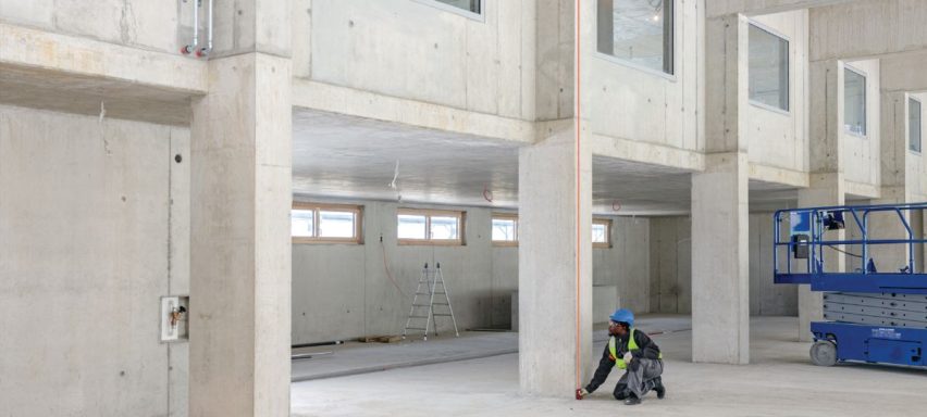 Obrero midiendo en un espacio de construcción con paredes de concreto y un andamio.