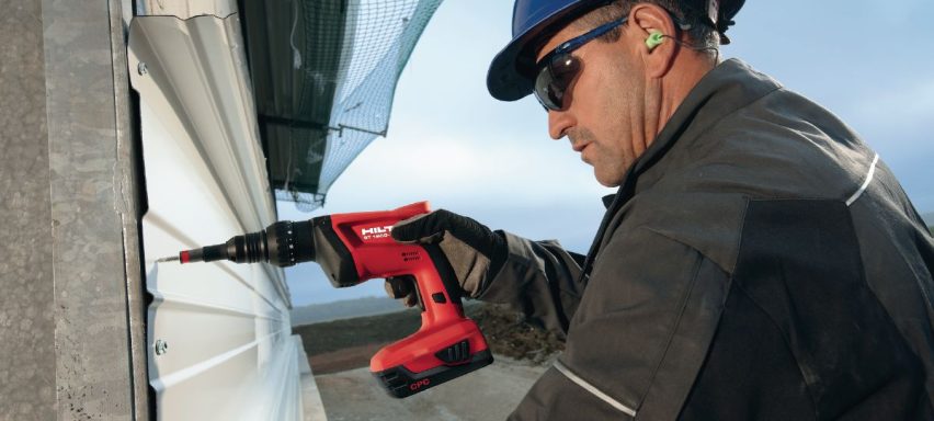 Trabajador usando un taladro eléctrico en una construcción al aire libre.