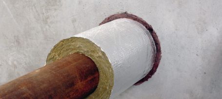 Tubería de metal con aislamiento en un agujero en la pared gris.