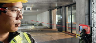 Hombre en casco y gafas de seguridad, usando un dispositivo con láser en obra en construcción.