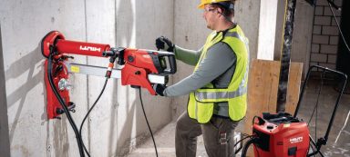Trabajador usando una herramienta eléctrica roja para perforar en una pared de concreto.
