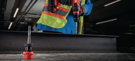 Persona usando una herramienta eléctrica en un entorno industrial. Lleva un chaleco de seguridad.