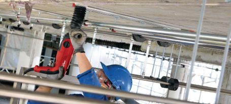 Trabajador con casco azul usando una herramienta eléctrica en un ambiente de construcción.