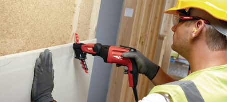 Hombre con casco y guantes utilizando una herramienta eléctrica en una pared.