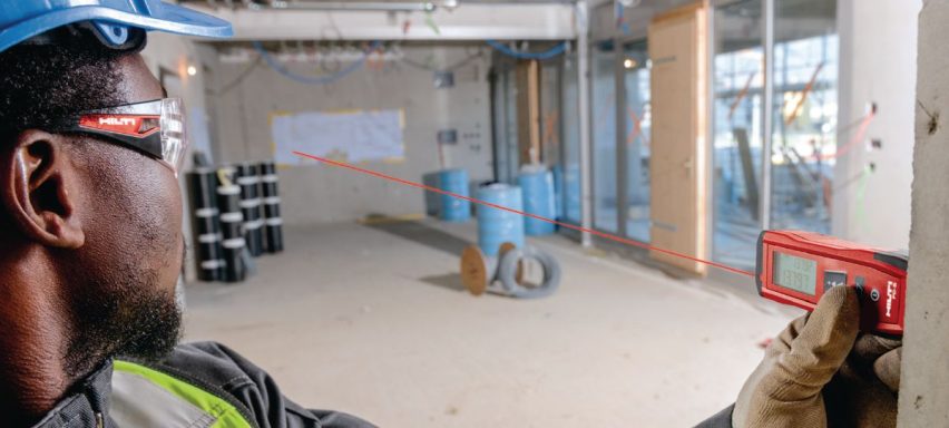 Hombre con casco y gafas usando un láser de medición en un espacio de construcción.