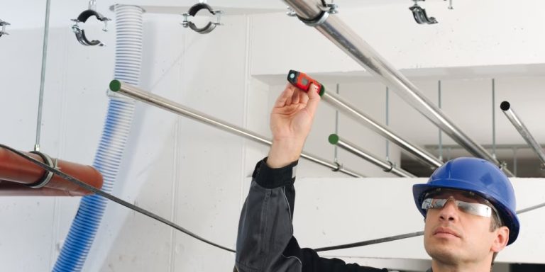 Trabajador con casco y gafas ajustando tuberías en un techo.