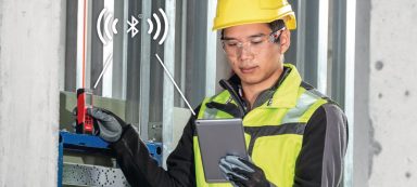 Hombre con casco y chaleco de seguridad usando una tablet en un entorno de construcción.