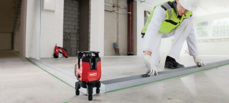 Un trabajador midiendo en el suelo con una herramienta láser en un entorno de construcción.