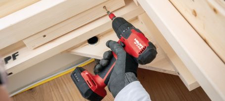 Persona usando un taladro inalámbrico rojo y negro en una superficie de trabajo de madera.