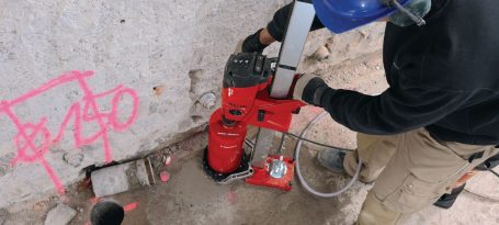 Herramienta eléctrica roja perforando una pared de concreto en una construcción.