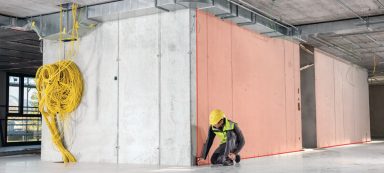 Obrero con casco amarillo trabajando en la construcción, cerca de una pared de concreto.
