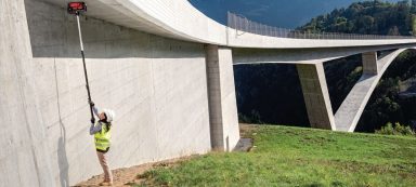 Trabajador en un puente de concreto, usando una manguera alta para limpiar o inspeccionar.