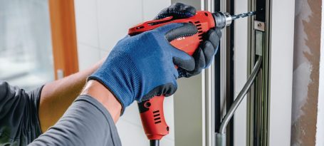 Persona utilizando un destornillador eléctrico rojo, con guantes, en un marco de puerta.