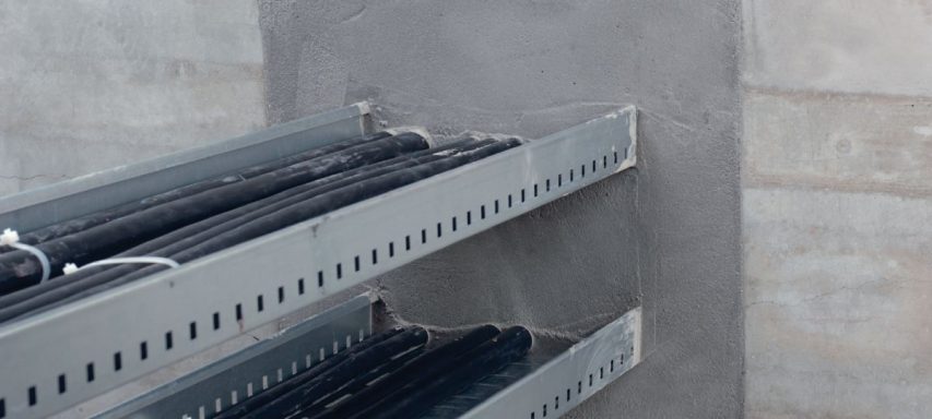 Estantes metálicos con rollos de cable negro sobre un fondo de cemento gris.