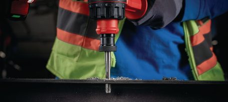 Mão usando un taladro eléctrico en una superficie metálica.