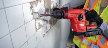 Trabajador con taladro perforando azulejos en una pared muy desgastada.